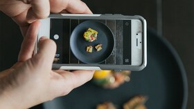 Некто фотографирует блюдо с изысканными продуктами