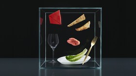 Столовые приборы, тарелки и продукты в стеклянном кубе, символизирующие принцип «Восприятие» программы обогащения вкуса.