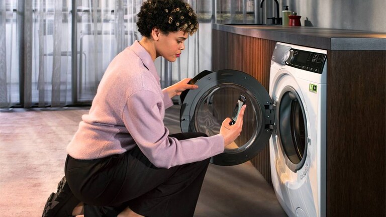 Woman looking at phone while opening a washing machine